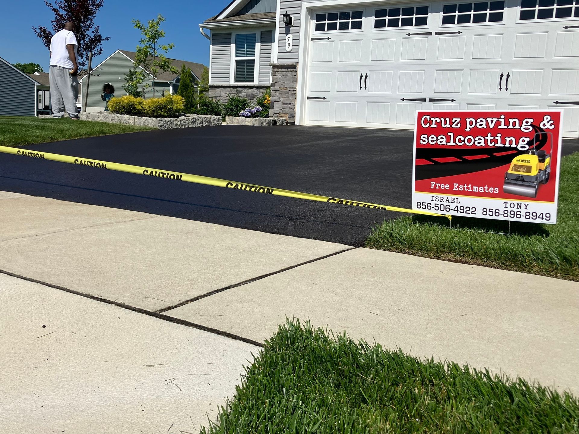 Newly paved driveway beside a garage, with a red sign for Cruz Paving & Sealcoating on a green lawn