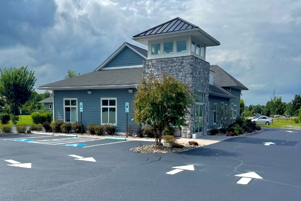 Stone-and-blue building with a tower in a parking lot with white directional arrows, under a cloudy sky