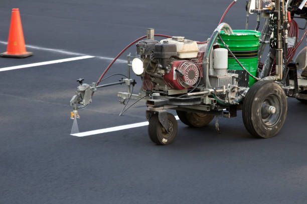 line striping machine spraying white painted lines in asphalt parking lot near an orange traffic cone