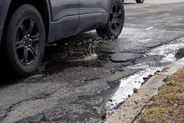 Car tire hitting a deep pothole on a cracked road, splashing water beside the curb