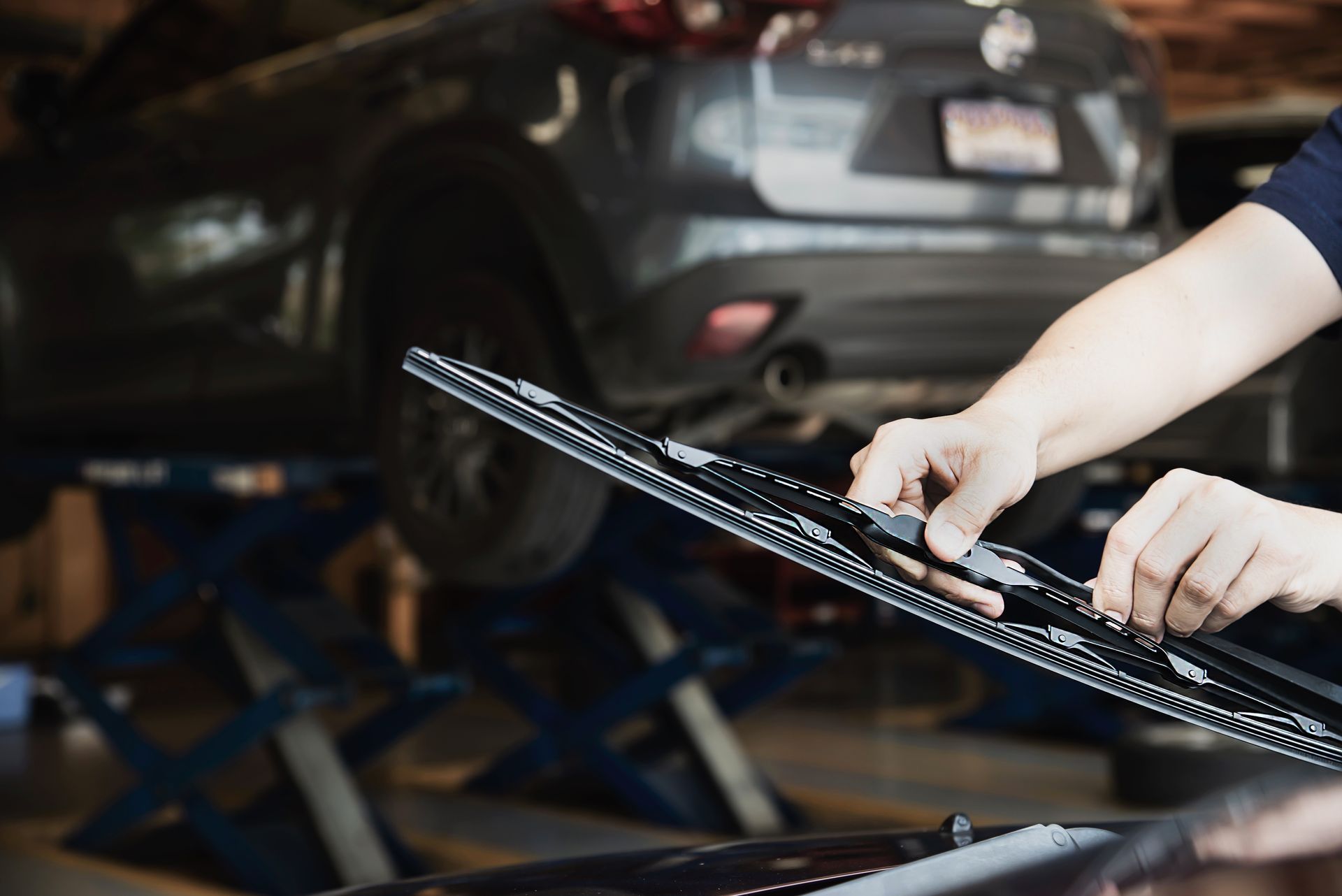 A person is changing a windshield wiper on a car in a garage | Quality Auto Electric & Repair