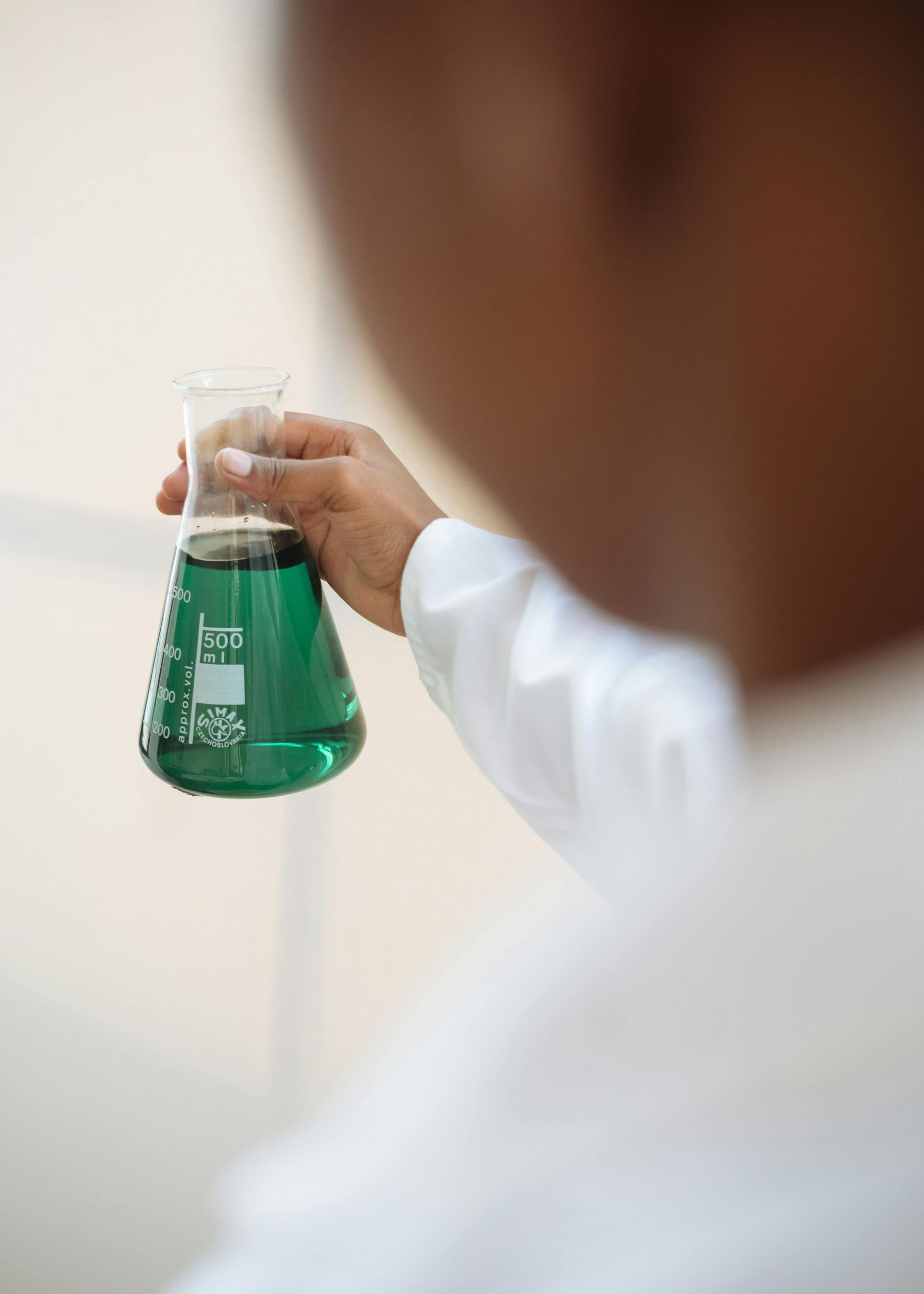 Person in lab coat holding a green liquid in a glass beaker.