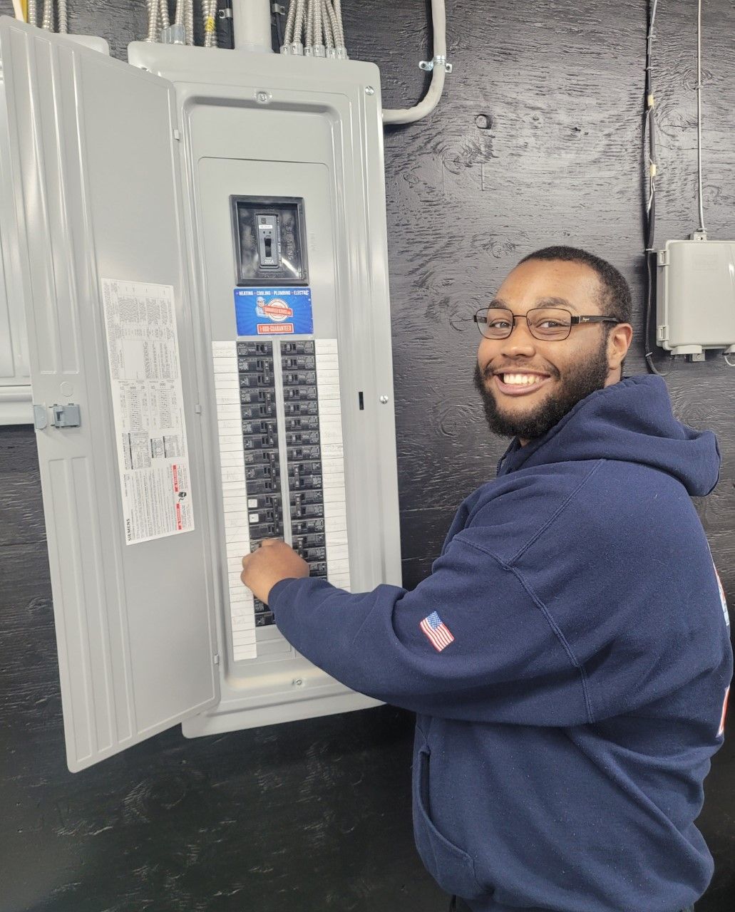 A man in a blue hoodie is working on an electrical panel.