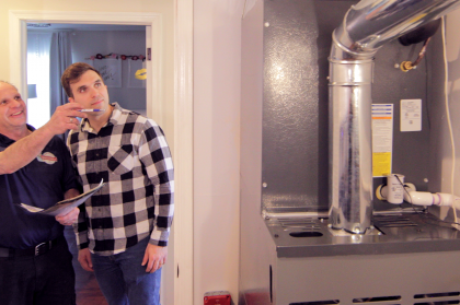 Two men are standing next to a heater in a room.