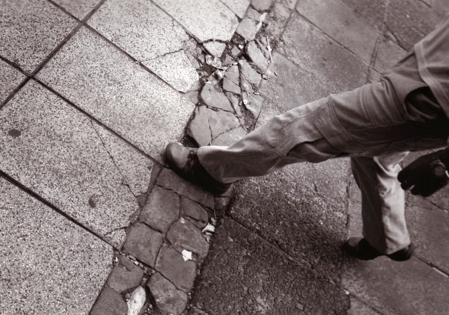 Close-up of a man stepping on cracked, damaged sidewalk