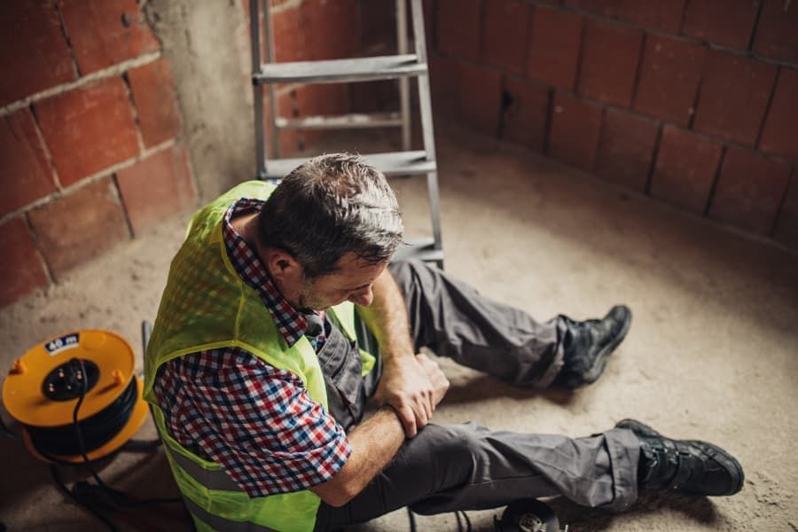Construction worker sitting on floor holding wrist after falling off ladder. 