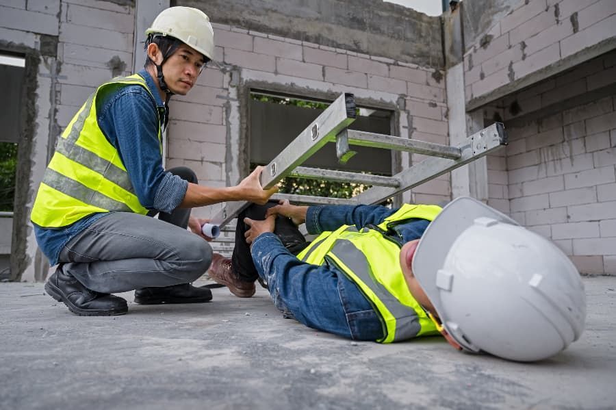 Construction worker lifting ladder off coworker who has fallen