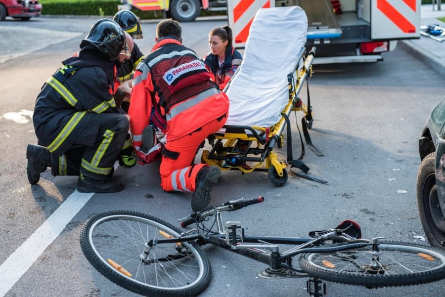 Firefighters and paramedics treating injured cyclist with damaged bicycle in the foreground. 