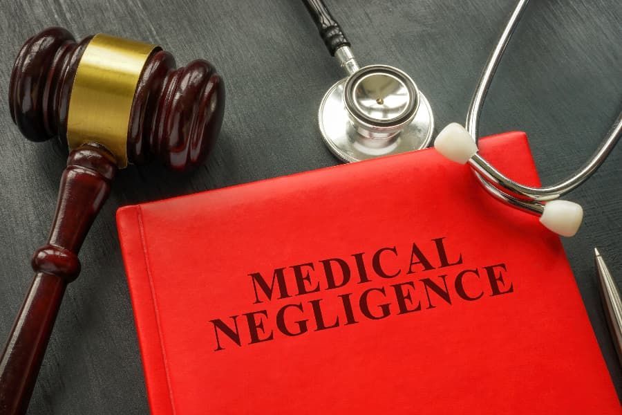 Wrecked bicycle, helmet, and eyeglasses on road in front of white car Gavel, stethoscope, and book titled “Medical Negligence.”