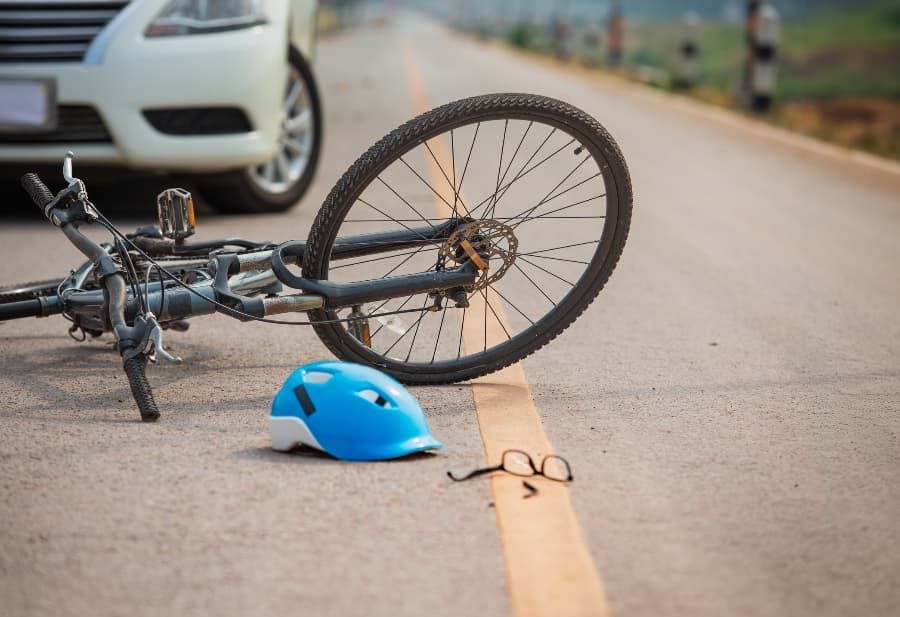 Young woman frowning and holding neck near wrecked white SUV Wrecked bicycle, helmet, and eyeglasses on road in front of white car