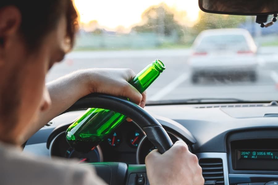 Young man driving with beer bottle in hand. 