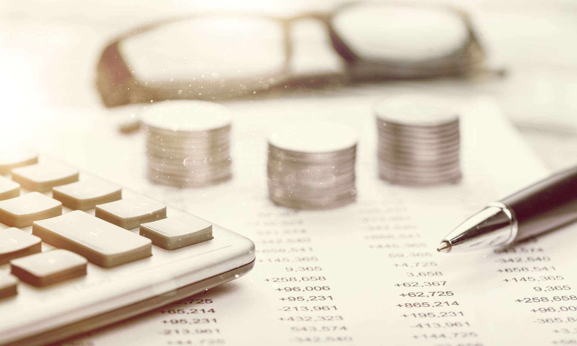 Close-up of a calculator next to a pair of piles of coins and a document.