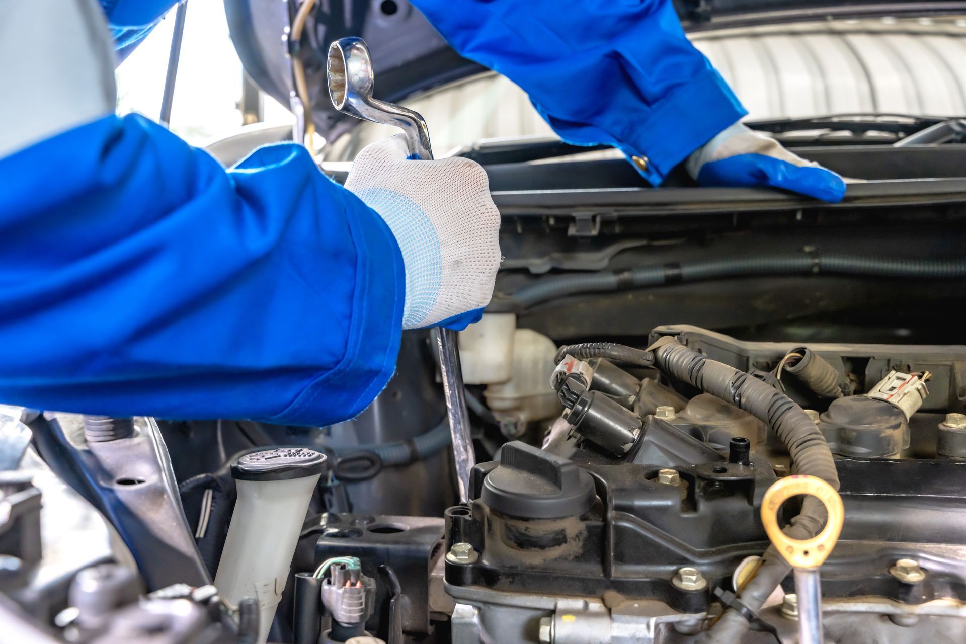 Mechanic in blue coveralls with gloves working on a car engine | Varsity Auto Repair and Tow LLC