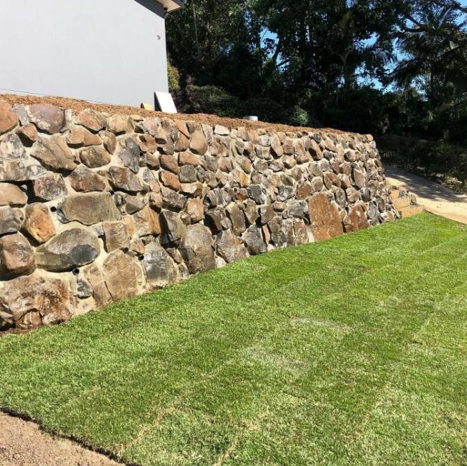 A Stone Wall Surrounds a Lush Green Lawn — Webster Rock Walls In Caboolture, QLD