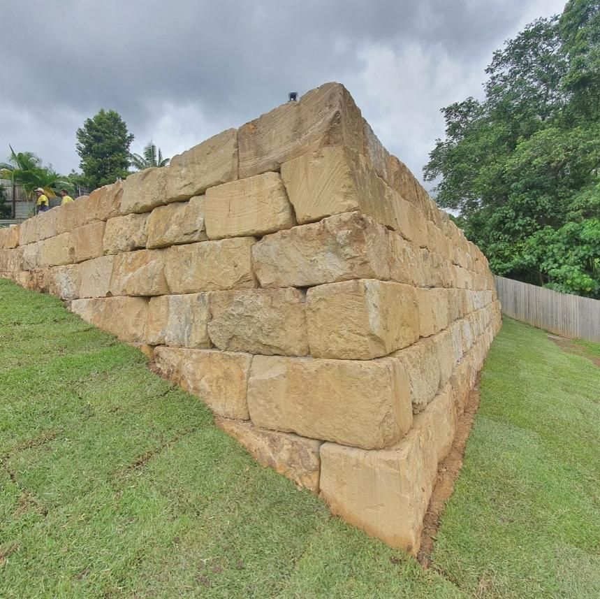 A Large Stone Wall Is Sitting on Top of A Grassy Hill — Webster Rock Walls In Caloundra, QLD