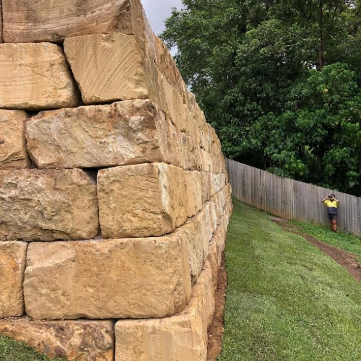 A Man Is Standing Next to A Large Stone Wall — Webster Rock Walls In Noosa, QLD