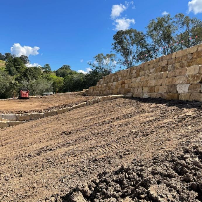 A Large Stone Wall Is Being Built in The Middle of A Dirt Field — Webster Rock Walls In Maroochydore, QLD