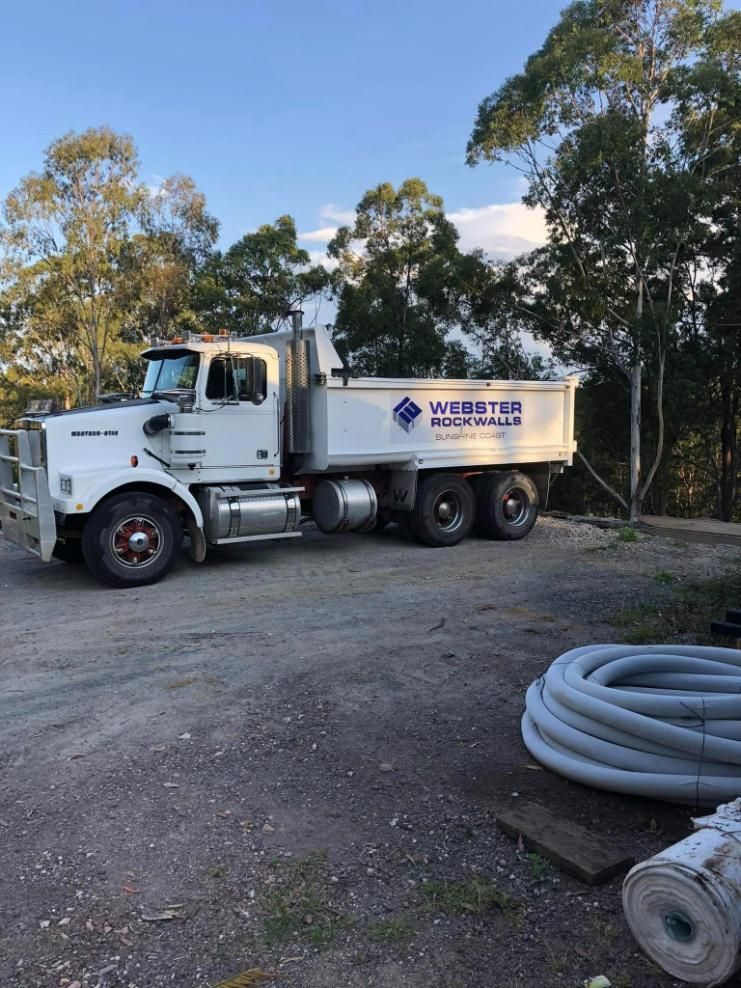 A White Dump Truck Is Parked in A Dirt Lot Next to Trees — Webster Rock Walls In Ilkley, QLD