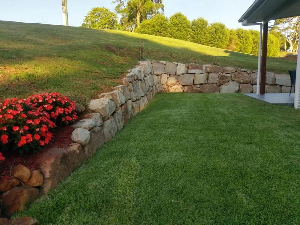 A Lush Green Yard with A Stone Wall and Flowers — Webster Rock Walls In Noosa, QLD