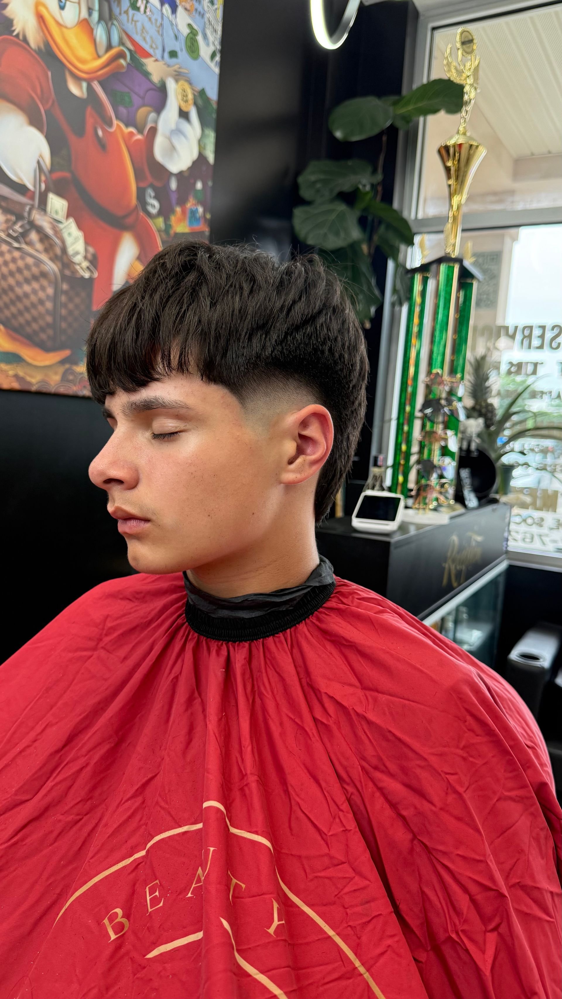 Young person with a fresh haircut, wearing a red cape, in a barbershop.