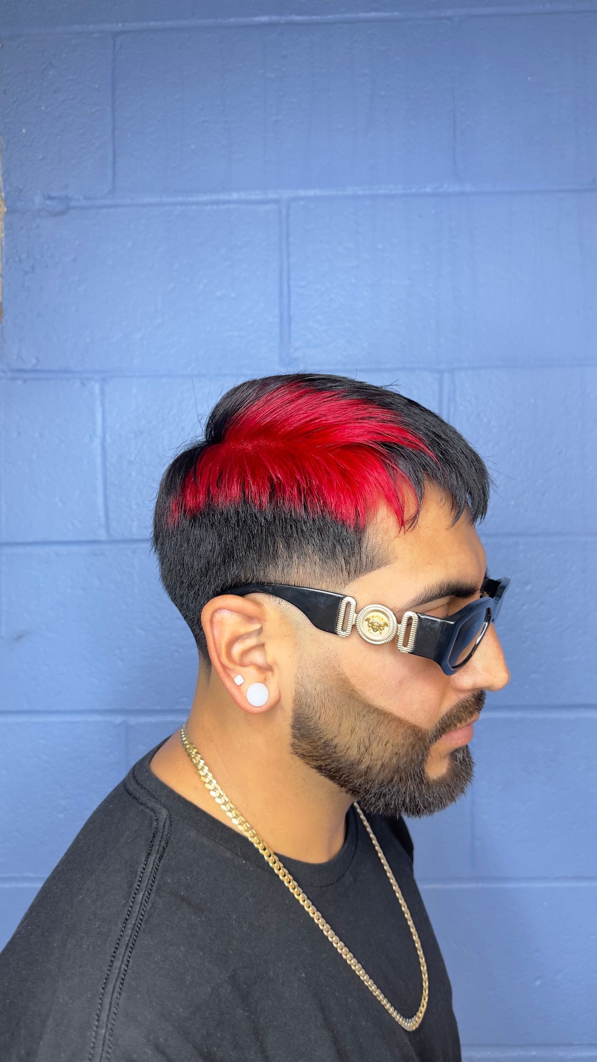 Man with black hair, red highlights, and sunglasses. He has a beard and is wearing a gold chain.
