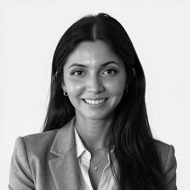 Woman with dark hair, smiling, wearing a blazer and button-down shirt.
