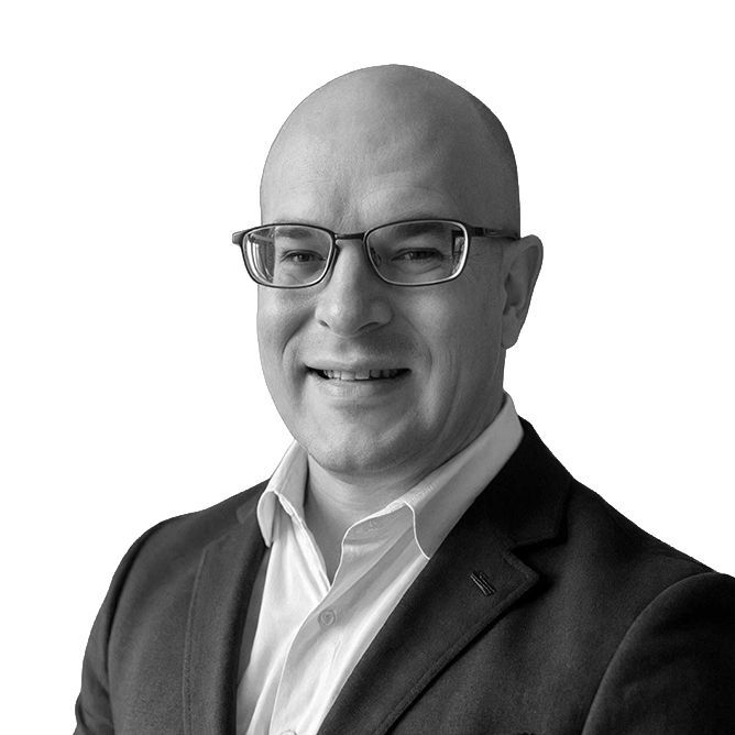 Bald man with glasses, wearing a suit jacket and white shirt, smiling.