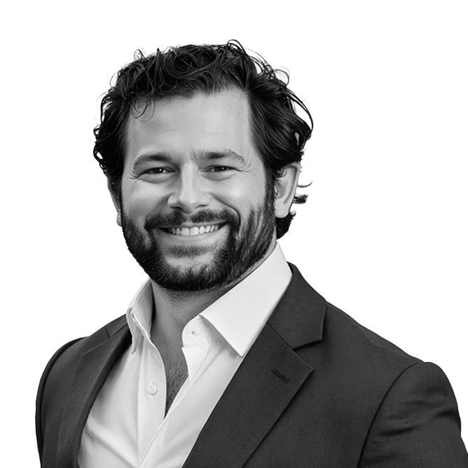 Man in a blazer and open-collared shirt smiles at the camera. Black and white photo.