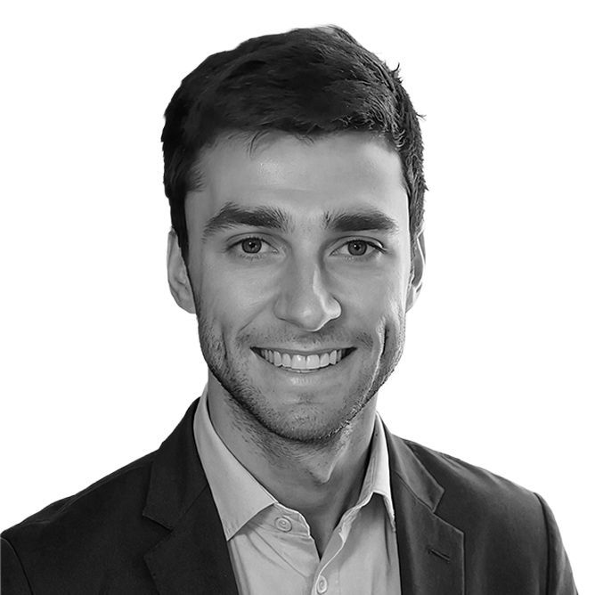 Smiling man in a suit jacket, facing the camera against a white background.