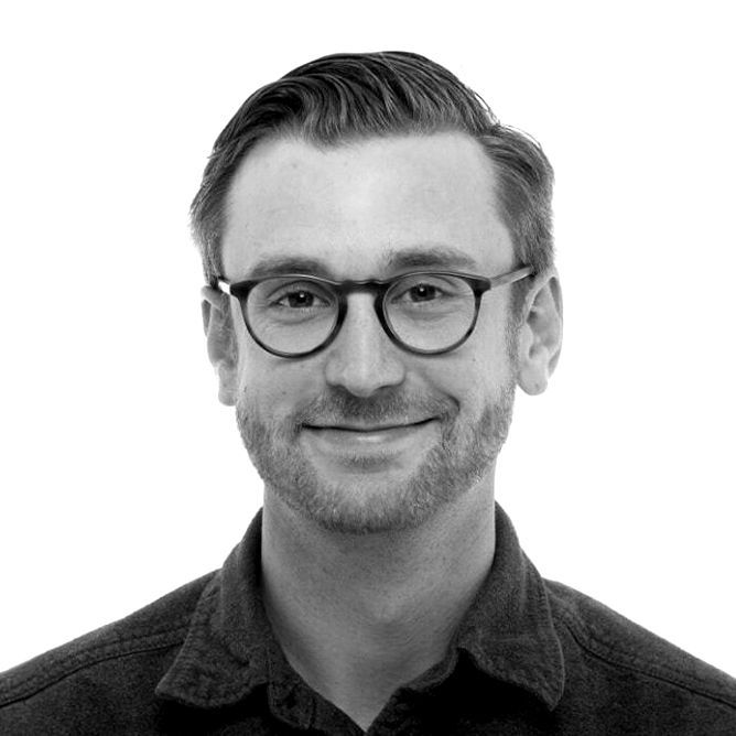 Man wearing glasses smiles, looking forward; close-up, grayscale.