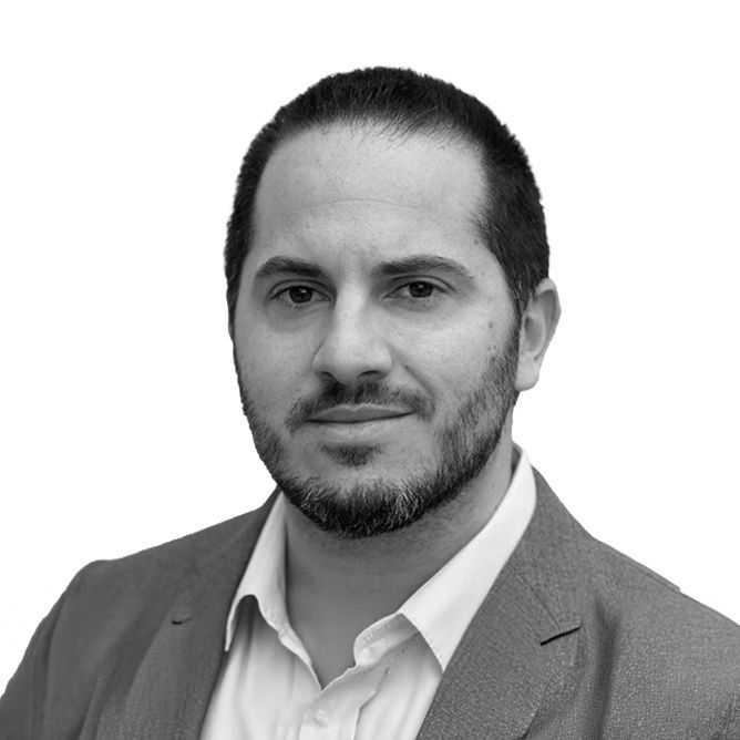 Man in suit and open-collared shirt looking at the camera. Black and white.