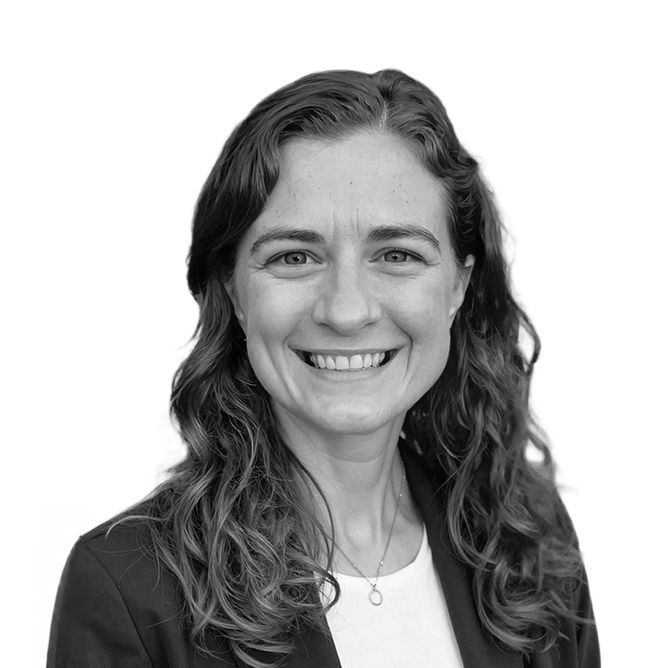 Woman with wavy hair smiling, wearing a blazer and white top, headshot.