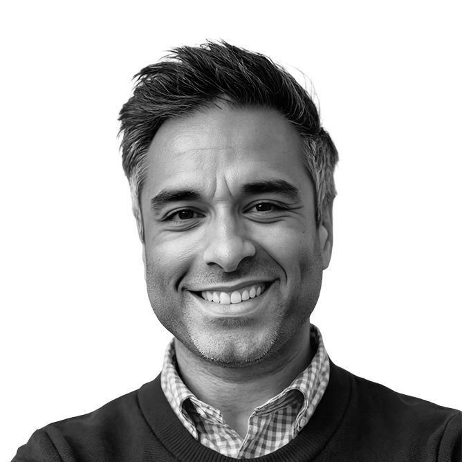 Man smiling, wearing a sweater and collared shirt. Black and white photo.