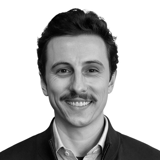 Man with dark hair and mustache smiling in black and white.