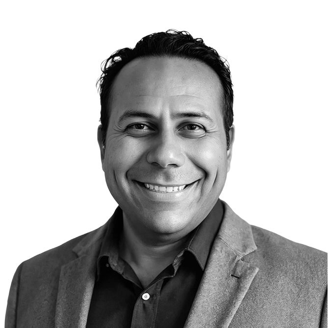 Smiling man in blazer, dark shirt. Gray tones, studio headshot.