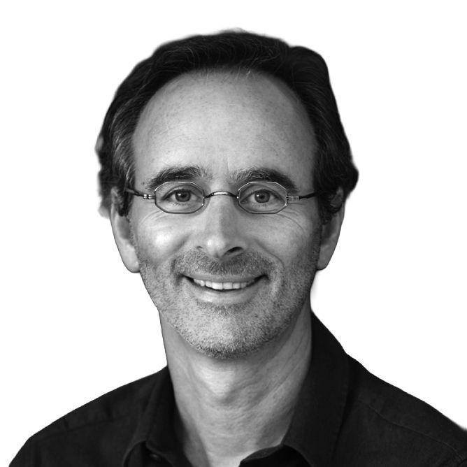 Man with glasses smiling, wearing a dark shirt, head and shoulders portrait.