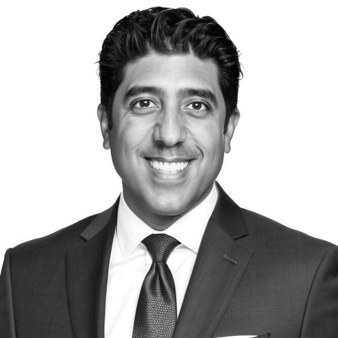 Man in suit smiles at the camera, against a white backdrop.