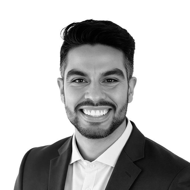 Smiling man in a suit jacket, white shirt, and trimmed beard. Studio shot, chest up.