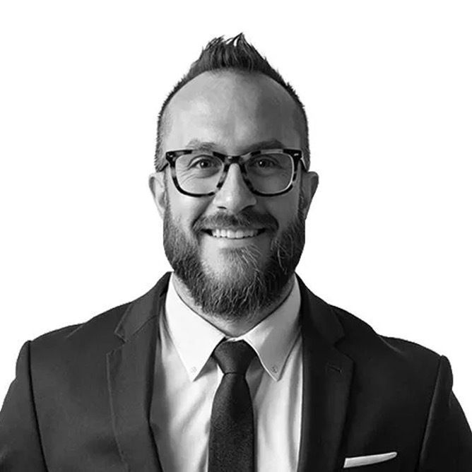 Man in suit and glasses smiles, with dark beard and hair, white background.