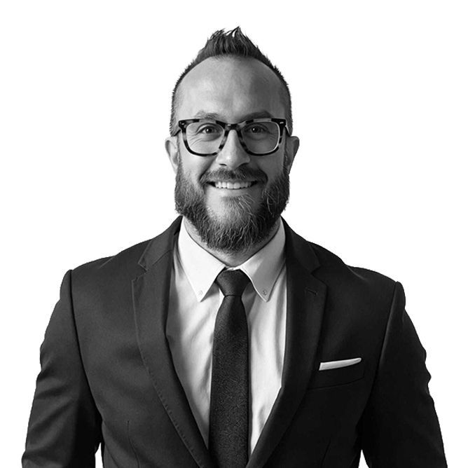 Man in suit and glasses smiles, with dark beard and hair, white background.