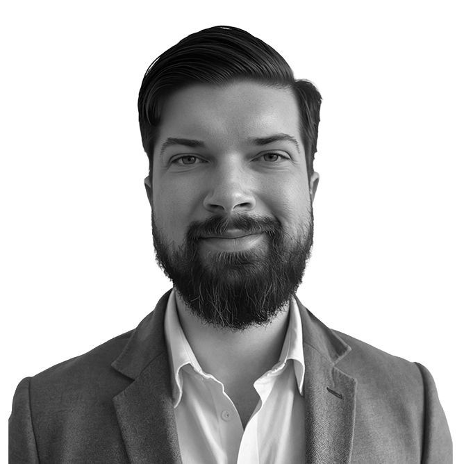 Man with a beard and dark hair wearing a blazer and open-collared shirt, smiling.