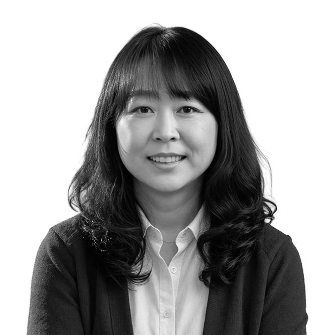 Woman with dark hair smiles, wearing a button-up shirt and a cardigan, against a white background.