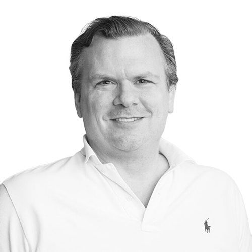 Man wearing a polo shirt smiles at the camera. Black and white, studio shot.