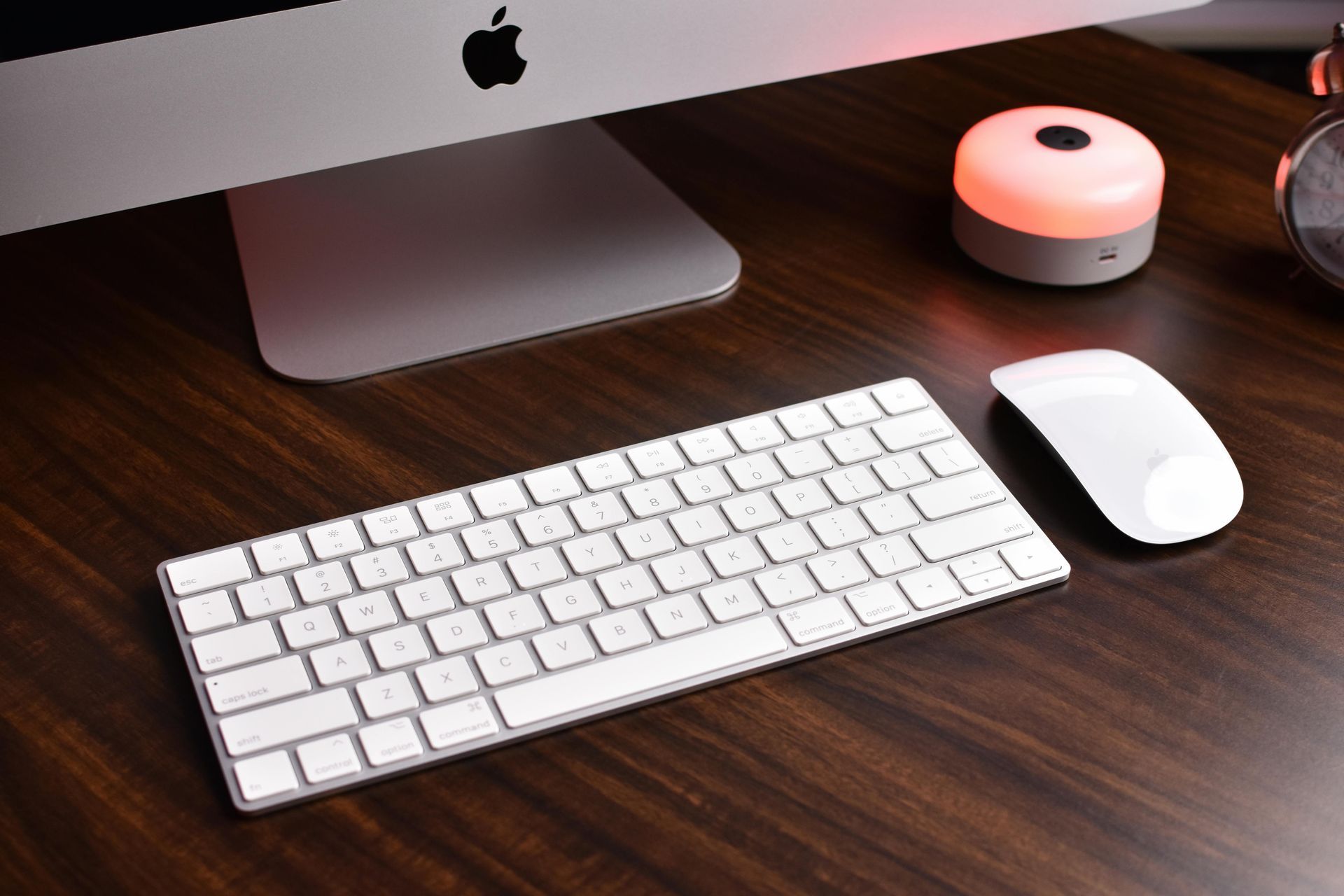 Apple computer setup on a wooden desk with keyboard, mouse, and light.