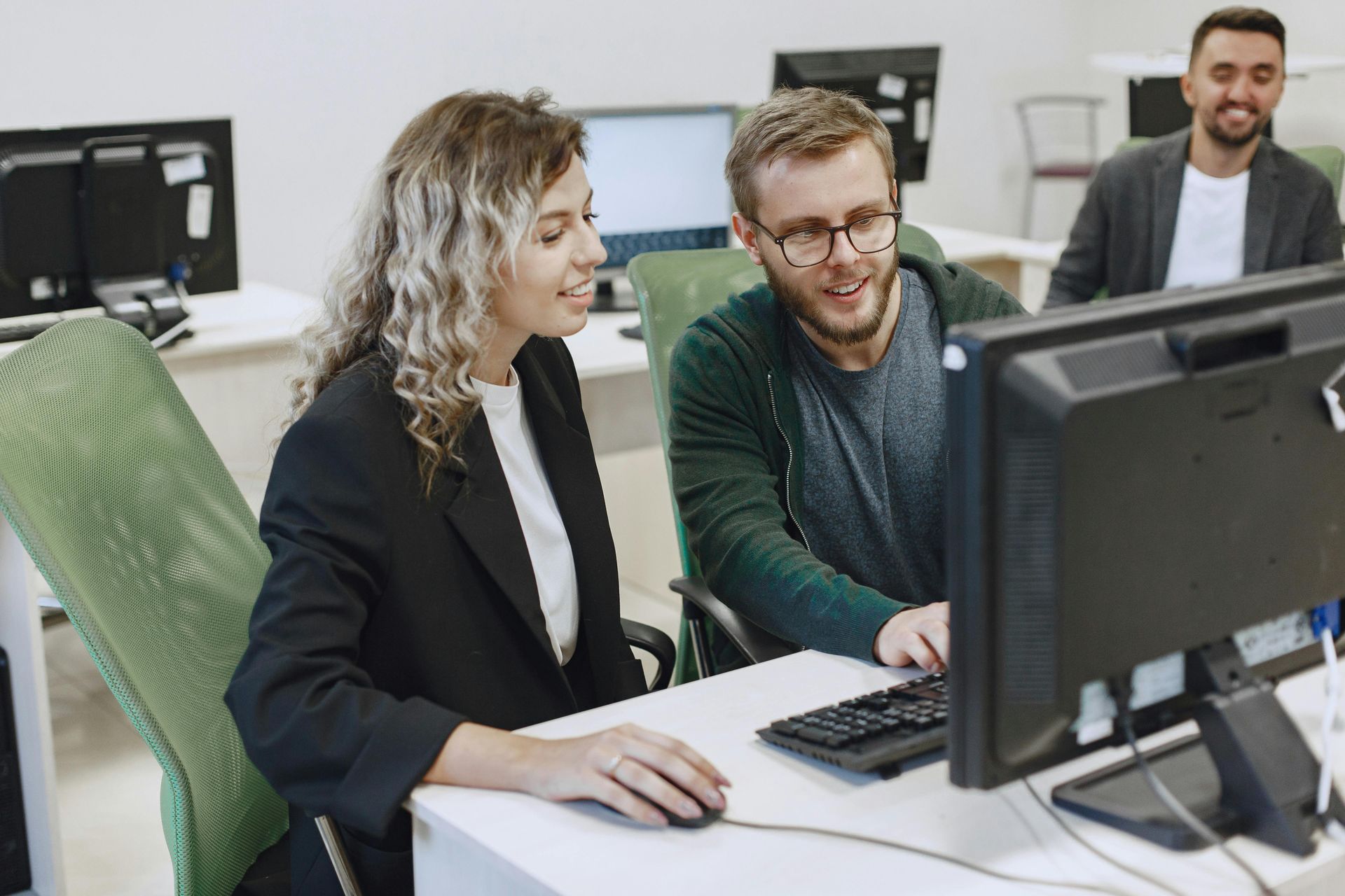 People collaborating at computers in an office, with one man pointing at a monitor.