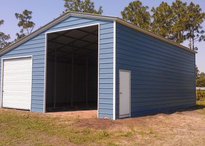A blue garage with a white door is sitting in the middle of a grassy field.