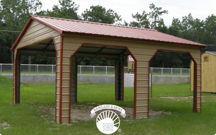 A metal carport with a red roof is in a grassy field