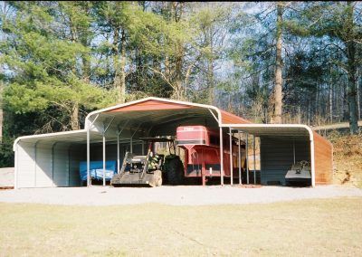 A red tractor is parked under a carport
