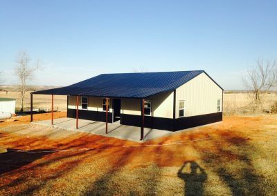 A large metal building with a black roof and a porch.
