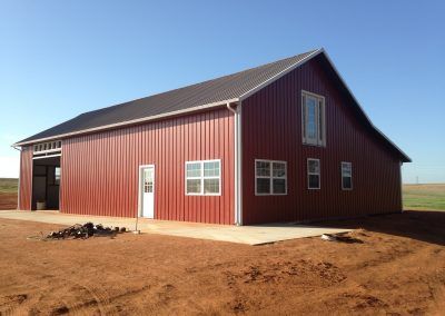 A large red barn is sitting in the middle of a dirt field.